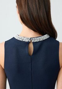 Abito navy con colletto di perline e scollatura a chiave nella parte posteriore. Texture liscia e design aderente.