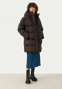 Brown puffer coat with a hood, horizontal quilted design, front zip closure, and side pockets, paired with a blue denim skirt and black boots.