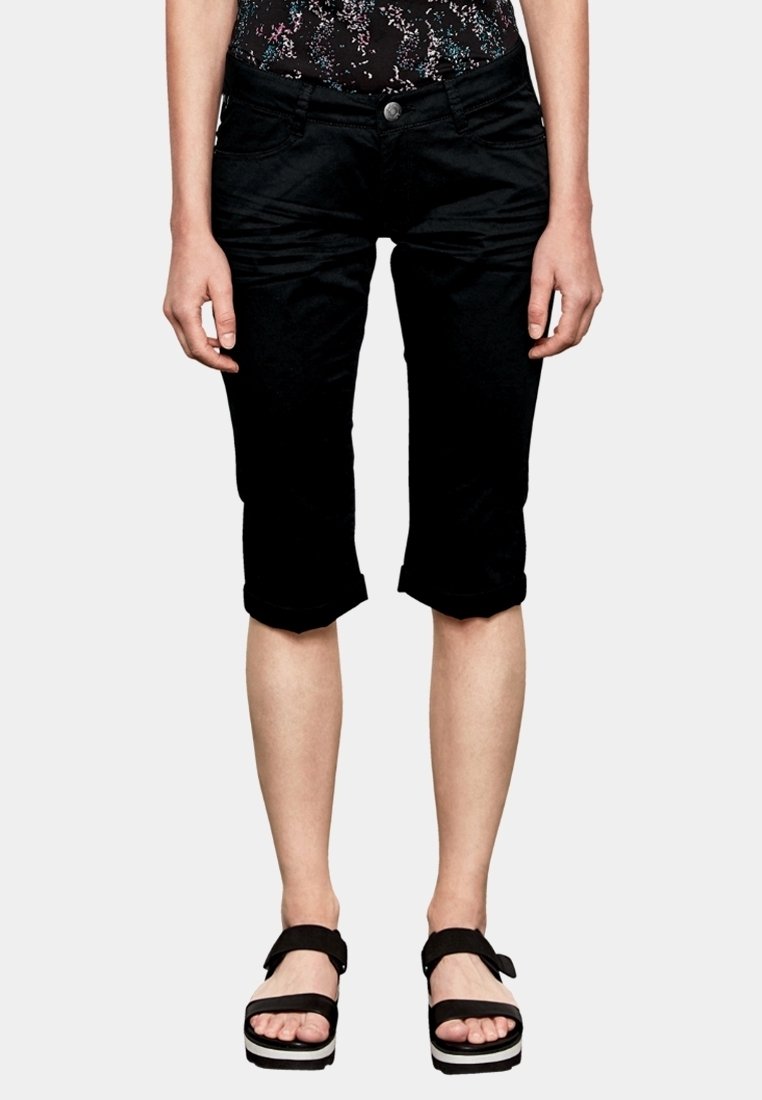 Pantalon noir raccourci en tissu lisse avec revers roulés ; doté de poches avant et d'une fermeture par bouton. Porté avec des sandales à plateforme noires.