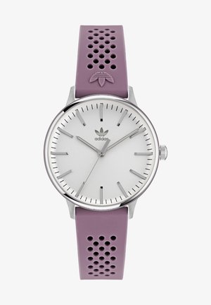 Violet perforuotas silikono dirželis su sidabriniu apvaliu ciferblatu, minimaliais žymekliais ir centruojančiu logotipu. Nerūdijančio plieno korpusas su tekstūruotu paviršiumi.