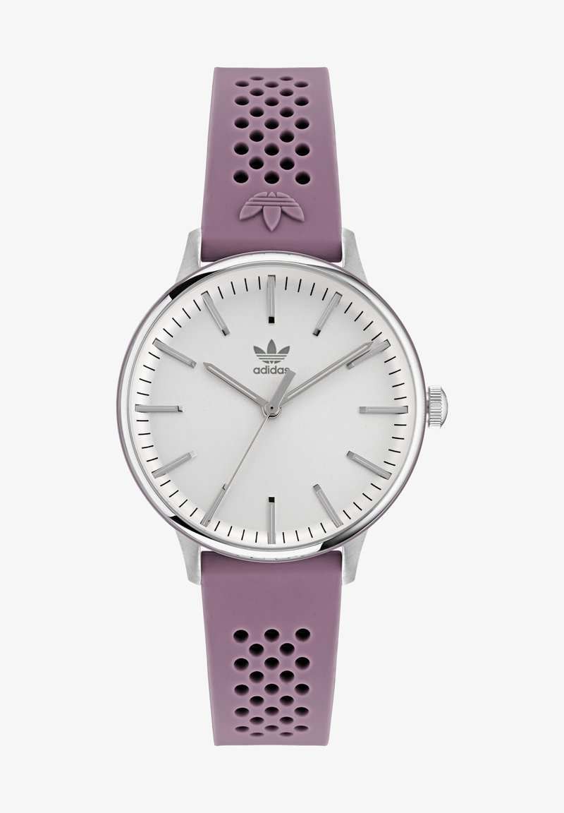 Lila perforerad silikonrem klocka med silverfärgad rund urtavla, minimala markeringar och centrerad logotyp. Kapsel i rostfritt stål med texturerad yta.