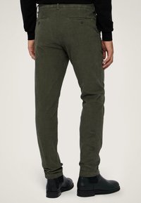 Olivgröna manchesterbyxor med slim fit. Har bakfickor med knappar och är tillsammans med svarta ankelstövlar. Slät textur.