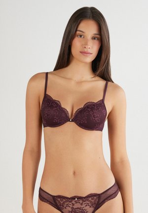 Soutien-gorge en dentelle bordeaux avec des bords festonnés et des armatures, présentant des motifs floraux décoratifs et des fines bretelles réglables. Culotte en dentelle assortie.