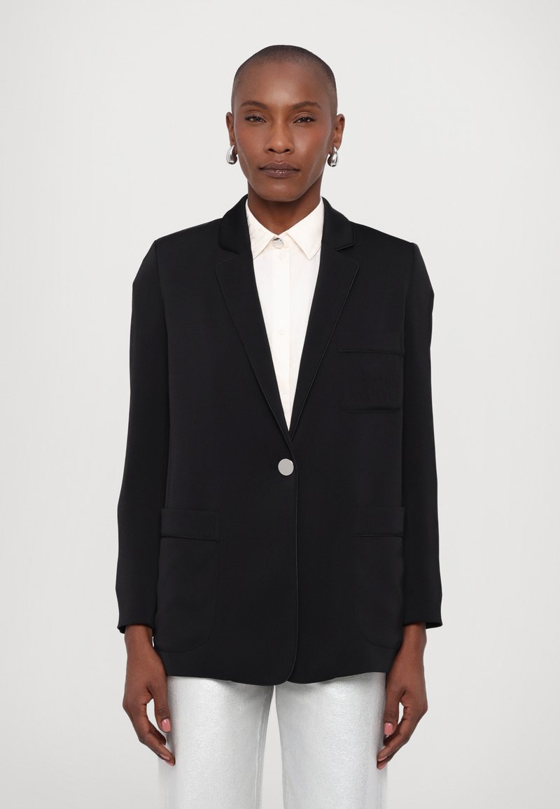 Blazer nero con colletto a punta, chiusura a un bottone, due tasche frontali e una tasca sul petto, abbinato a pantaloni argento.