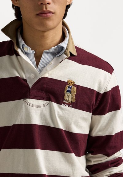 Burgunder og hvitstripet rugbyskjorte med krage, som har et brodert bjørnsdesign iført et blått skjerf og "POLO"-tekst på brystet.