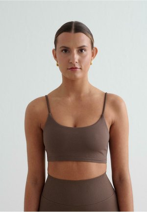 Brauner, kurz geschnittener Tanktop mit dünnen Trägern, aus weichem Material gefertigt. Glatte Textur mit tailliertem Design, kombiniert mit hochgeschnittenen passenden Unterteilen.