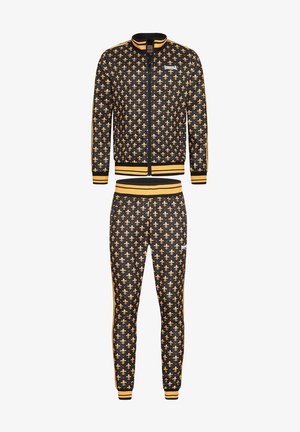 Black tracksuit with gold fleur-de-lis pattern, featuring a zip-up jacket with ribbed cuffs and waistband, matching tapered pants with similar design.