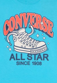 Lyseblå t-shirt med et grafisk motiv af en hvid sneaker, med "CONVERSE" i rød og "ALL STAR SINCE 1908" i mørkeblå under.