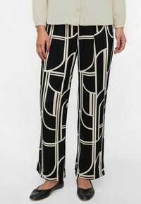 Pantalones anchos negros con un patrón geométrico en beige, con una textura de tela suave y un ajuste relajado. Combinados con zapatos planos negros.
