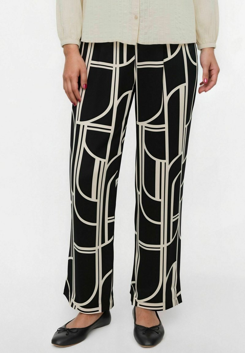 Pantalones anchos negros con un patrón geométrico en beige, con una textura de tela suave y un ajuste relajado. Combinados con zapatos planos negros.