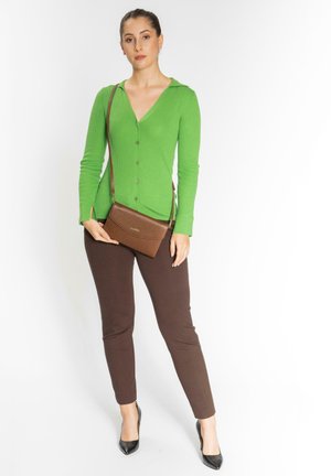 Bolso cruzado marrón con textura y correa larga, combinado con un cárdigan verde de canalé y pantalones ajustados marrones, completando un atuendo casual.