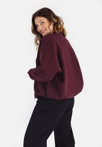 Bordowy, oversize sweatshirt z opuszczonymi ramionami, o miękkiej teksturze i ściągaczami, w połączeniu z czarnymi spodniami. Prosty, nowoczesny design.