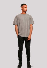 Gray oversized t-shirt with visible stitching, paired with black joggers. Model wears black athletic shoes. Plain background.