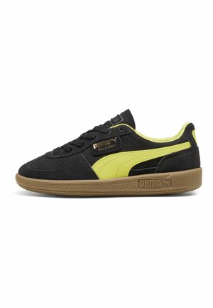 Baskets en daim noir avec des accents jaune vif, offrant une semelle en gomme texturée et une étiquette en or sur le côté, design bas classique.