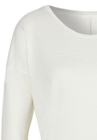 Weißes Langarmoberteil mit weiter Halslinie und strukturiertem Stoff. Mit überschnittenen Schultern und einem lässigen Schnitt.