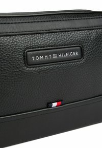 Schwarze, strukturiert genarbte Leder-Clutch mit rechteckigem Design, geprägt mit dem "TOMMY HILFIGER"-Logo und einem kleinen rot-weißen-blauen Akzent am Boden.