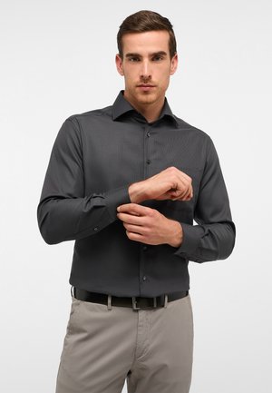 Dunkelgraues langärmliges Hemd mit subtiler Textur, Button-Down-Kragen und verstellbaren Manschetten, kombiniert mit hellbeigen Hosen und einem schwarzen Gürtel.