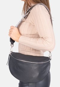 Schwarze Lederhandtasche mit einer genarbten Textur, geschwungener Form und silbernem Zubehör. Verfügt über einen gemusterten Trageriemen für zusätzliche Details.