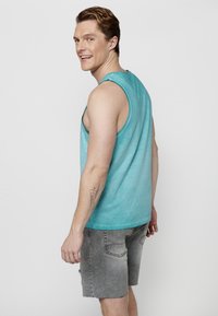 Turkos ärmlös topp med en avslappnad passform, i kombination med ljusgrå slitna shorts. Rå kant vid ärmhålen och en avslappnad design.