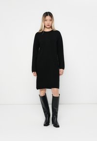 Abito lungo a maniche lunghe in maglia nera con scollatura rotonda, abbinato a stivali neri in pelle al ginocchio, texture liscia e vestibilità comoda.