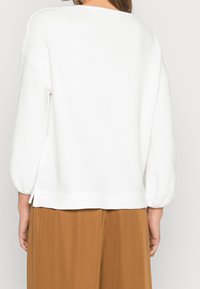 White, textured sweater with a relaxed fit, balloon sleeves, and a rounded neckline; features side slits at the hem.