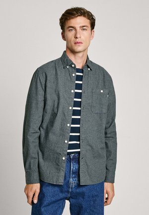 Gray flannel button-up shirt with a chest pocket, worn over a navy and white striped tee, paired with blue denim jeans.