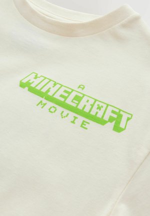 Cremefarbenes T-Shirt mit grüner, pixelierter Schrift "A MINECRAFT MOVIE." Aus glattem Baumwollstoff, mit rundem Ausschnitt und kurzen Ärmeln.