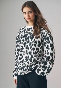 Felpa con stampa leopardata in bianco e nero, dalla vestibilità rilassata, con colletto a girocollo e maniche lunghe, abbinata a pantaloni scuri.