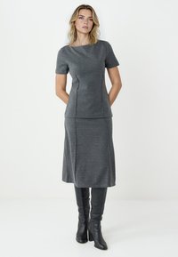 Graues Zweiteiler-Outfit, bestehend aus einem kurzärmeligen Oberteil mit rundem Ausschnitt und einem knielangen Rock, gefertigt aus strukturiertem Stoff. Schwarze knielange Stiefel.