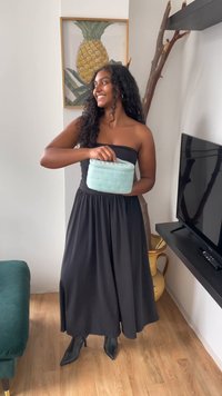 En lys aqua quiltet kosmetikkveske med et håndtak, holdt av en person i en svart stroppeløs kjole, mot en nøytral bakgrunn.