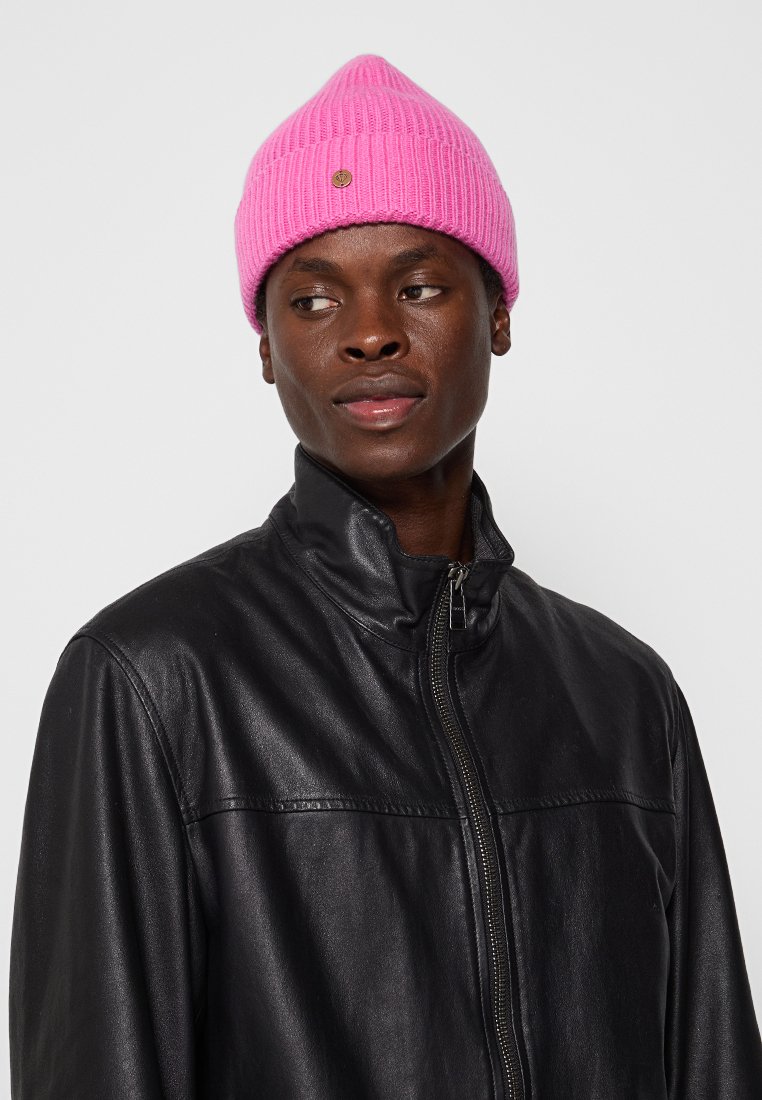 Różowy dzianinowy beret o prążkowanej fakturze z akcentem w postaci logo. Noszony z czarną skórzaną kurtką z wysokim kołnierzem i zamkiem błyskawicznym.