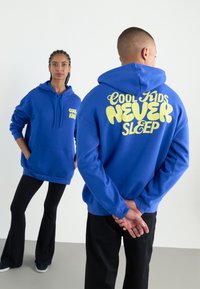 Blue hoodie made of cotton blend. Features front pocket, drawstring hood, and bold yellow text on back: "COOL KIDS NEVER SLEEP."
