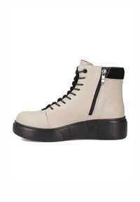 Beżowe skórzane botki za kostkę z czarną podeszwą, z czarnym sznurowanym wzorem, bocznym zamkiem i teksturowanym czarnym akcentem u góry.