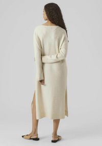 Robe en tricot crème à manches longues avec fentes latérales et un dos légèrement ouvert. Texture douce et coupe décontractée.