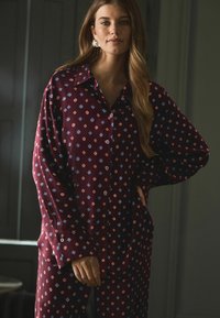 Koszula w kolorze wina o luźnym kroju, z geometrycznym wzorem w niebieskim i czerwonym. Długie rękawy i klasyczny kołnierzyk, wykonana z miękkiego materiału.