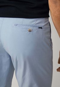 Ljusblå byxor med en bakficka som har ett knappstänge och en liten svart etikett. Slät tygkvalitet med en kroppsnära design.