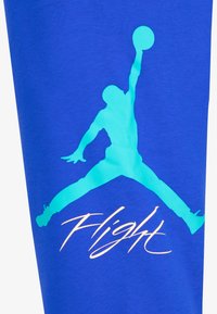 Silueta basketbalisty skákajícího s jednou rukou nataženou a držícího míč, nad slovem "Let" na modré tkanině.