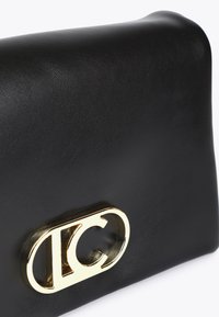 Svart läderclutch med ett böjt, glänsande guldspänne som har en stiliserad logotyp. Designen är slank och modern, vilket betonar elegans.