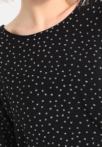 Top de tela negra con cuello redondo, que presenta un patrón repetido de pequeñas rayas blancas y plateadas en diferentes orientaciones.