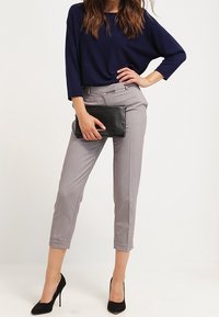 Námořnické modré volné tričko, šedé vypasované kotníkové kalhoty s ohrnutými manžetami, doplněné černými vysokými podpatky a černou kabelkou.