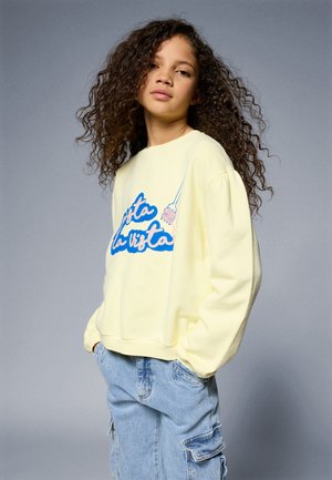 Geel sweatshirt met een blauwe opdruk met de tekst "Hasta la vista", voorzien van een speelse uitstraling en een relaxte pasvorm. Draagt met lichtblauwe cargobroek.
