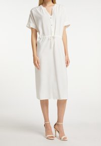 Weißes Midi-Kleid mit kurzen Ärmeln, einer Knopfleiste und einem elastischen Kordelzug in der Taille. Glatter Stoff mit lockerer Passform und knielanger Saum.