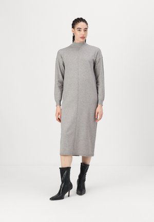 Robe sweat-shirt grise avec un col haut, des manches longues et des détails de couture verticaux, associée à des bottines à talons noires. Texture de tissu lisse.