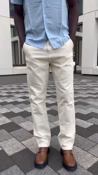 Camisa de manga curta azul clara, calças slim-fit creme, e sapatos de couro castanho com sola de borracha preta, de pé sobre um pavimento decorado.