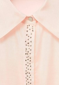 Blusa rosa chiaro con colletto a punta, dotata di una fila verticale di perline metalliche lungo la parte anteriore della placca dei bottoni.