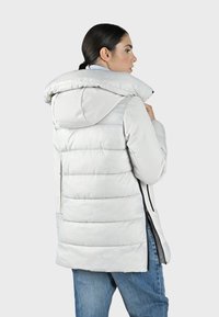 Chaqueta acolchada gris claro con capucha, con un diseño acolchado, un poco más larga por detrás y cremalleras a lo largo de los lados para ventilación.