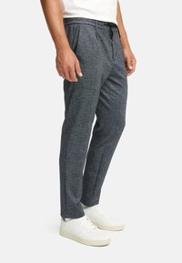 Sorte skreddersydde bukser med teksturert mønster, elastisk midjebånd og snor, kombinert med hvite joggesko.