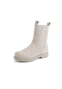 Bottines en suède beige avec des panneaux élastiques sur les côtés, des languettes de tirage et une semelle en caoutchouc texturé. Elles présentent un bout arrondi et un minimum de coutures.