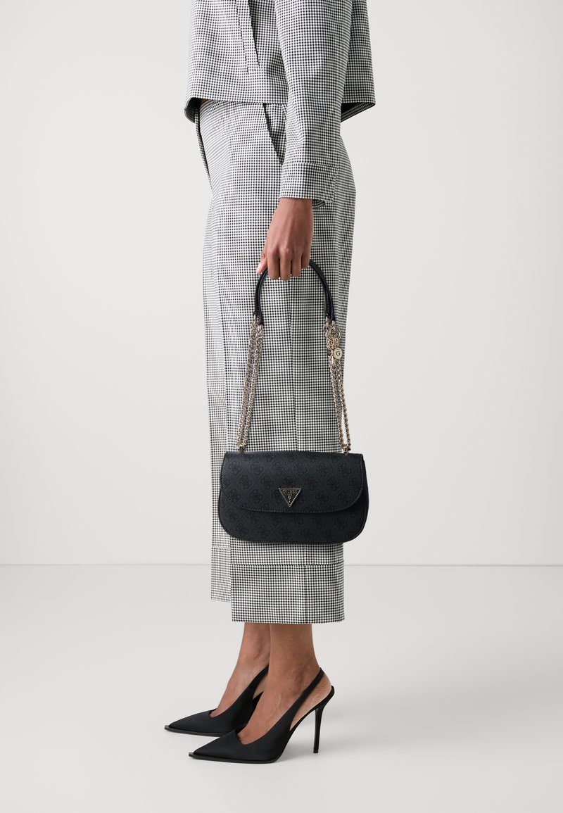 Borsa nera strutturata con forma curvata, tracolla in catena dorata e accentuazione del logo. Indossata con pantaloni a scacchi grigi e tacchi neri.