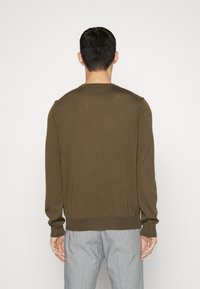 Mörk olivgrön tröja med långa ärmar och rundad hals. Ribbad fåll och ärmslut. Slät textur, figurnära passform. Bärs över grå byxor.